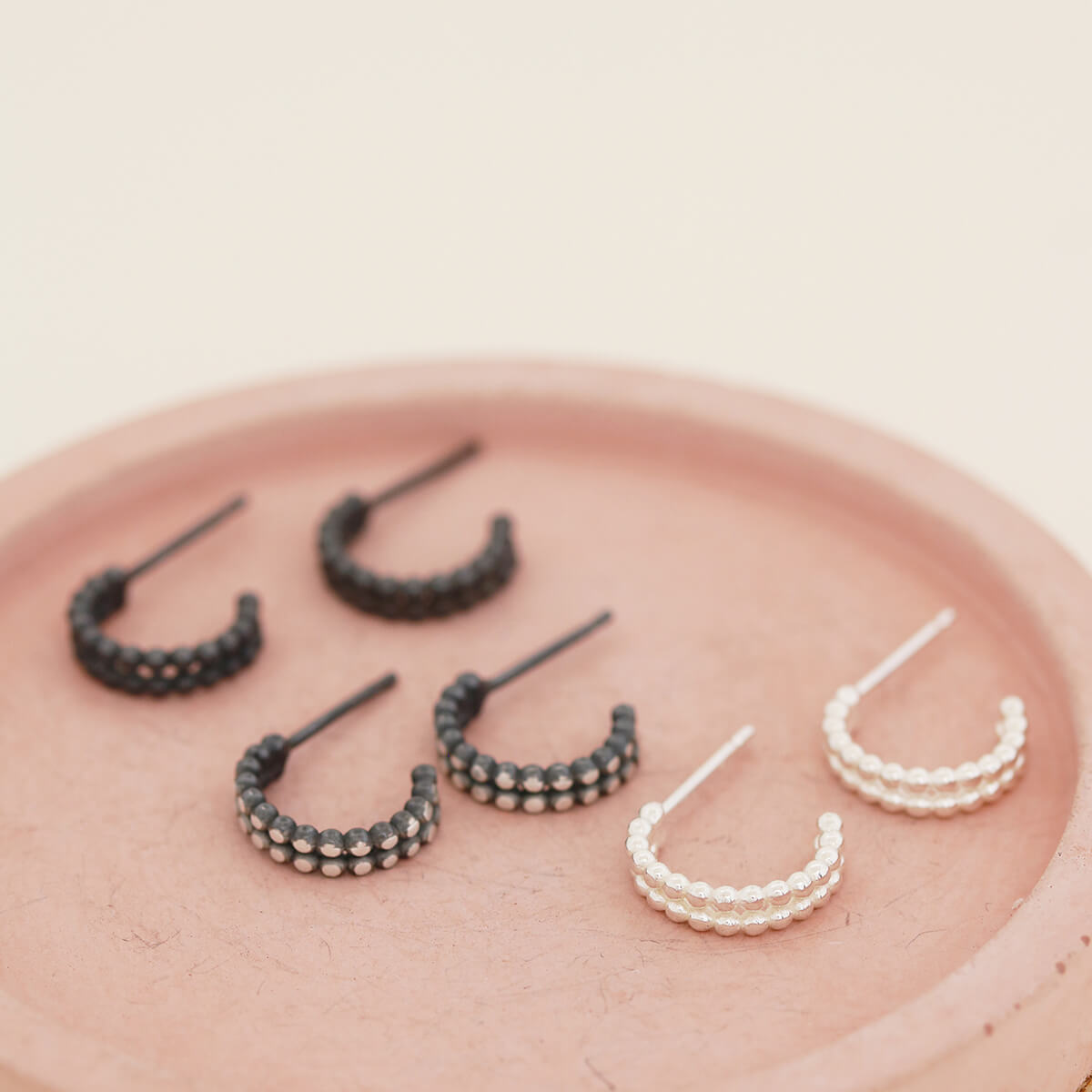 Silver and black hoop earrings shown alongside silver and black finishes on a pink dish