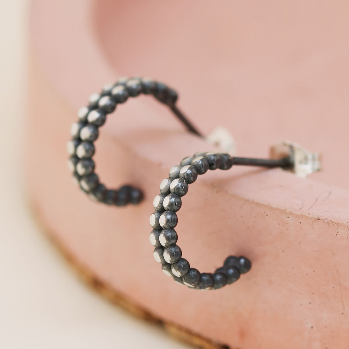 Silver and black hoop earrings arranged on a pink dish, modern small hoop earrings
