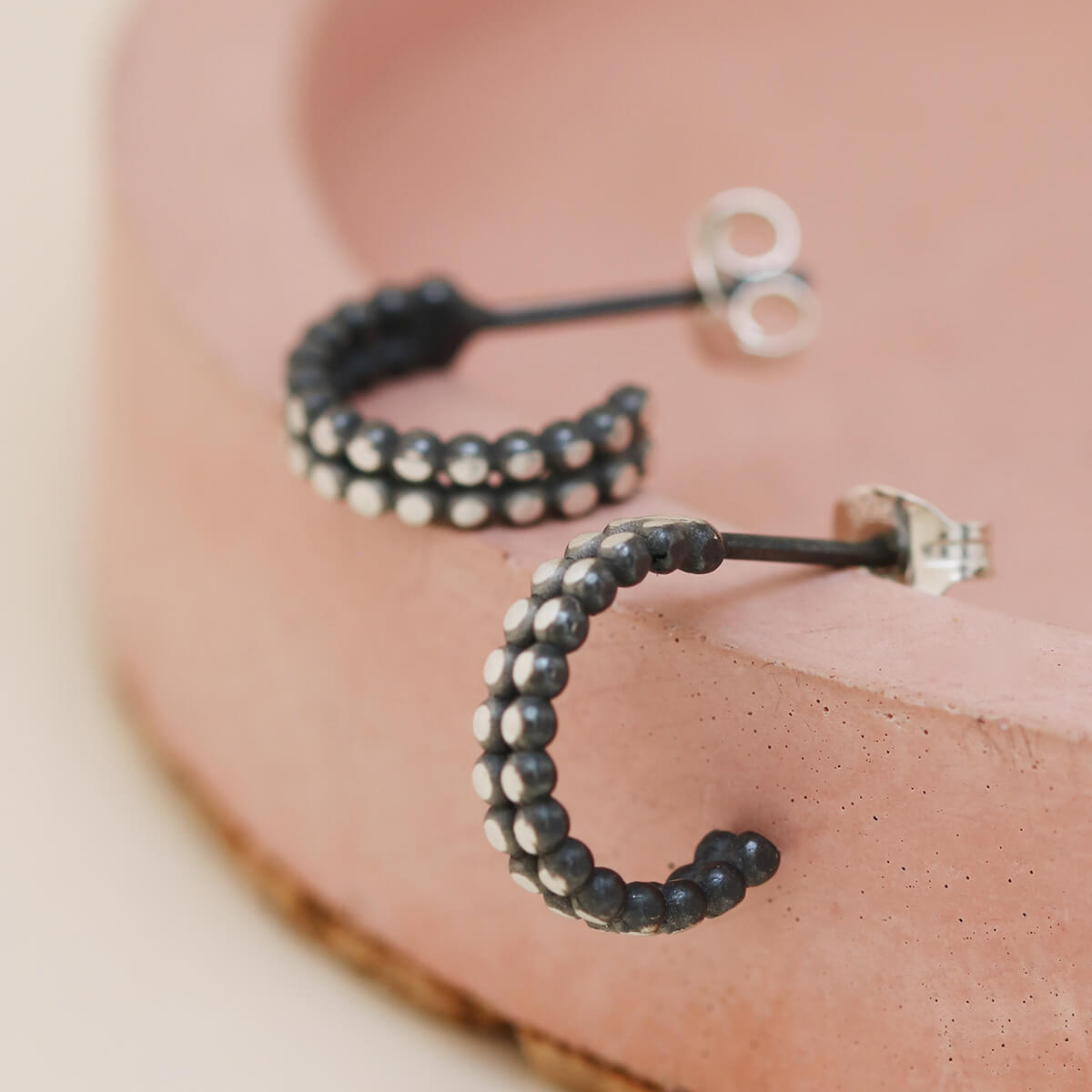 Close up of silver and black hoop earrings on a pink dish, modern little black hoop earrings