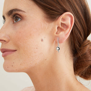Long black pearl earrings modelled to show their elegant elongated silhouette and comfortable stud fitting. 