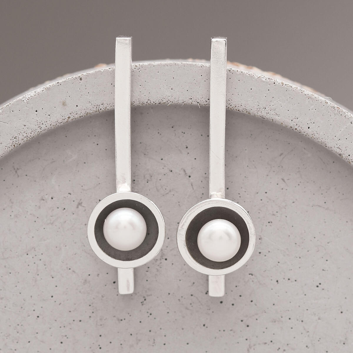 Handmade long black pearl earrings in oxidised sterling silver with genuine freshwater pearls displayed on a grey ceramic dish.