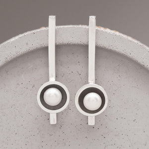 Handmade long black pearl earrings in oxidised sterling silver with genuine freshwater pearls displayed on a grey ceramic dish.