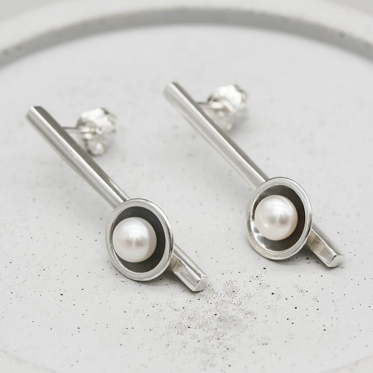 geometric design.
Long black pearl earrings handcrafted in sterling silver with oxidised finish and freshwater pearls, displayed on a grey dish.