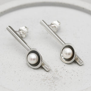 geometric design.
Long black pearl earrings handcrafted in sterling silver with oxidised finish and freshwater pearls, displayed on a grey dish.
