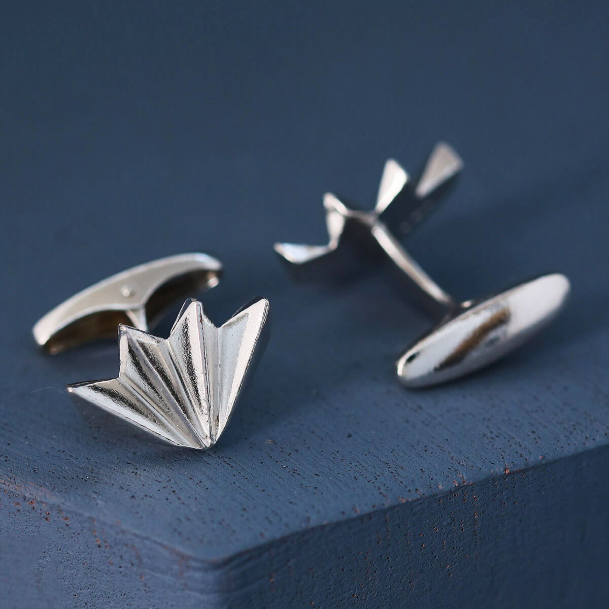 Close-up of geometric art deco cufflink face on deep blue background showing crisp fan texture, stylish men’s silver cufflinks for formal wear