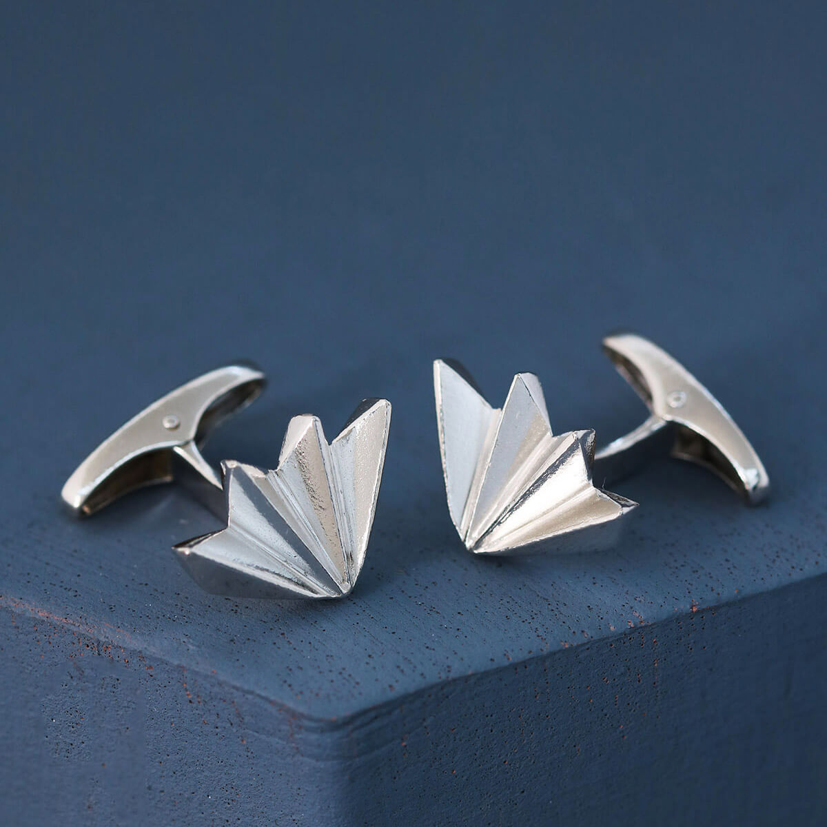 Set of art deco cufflinks resting on deep blue background, elegant men’s silver cufflinks handmade in the UK, perfect luxury gift for dad