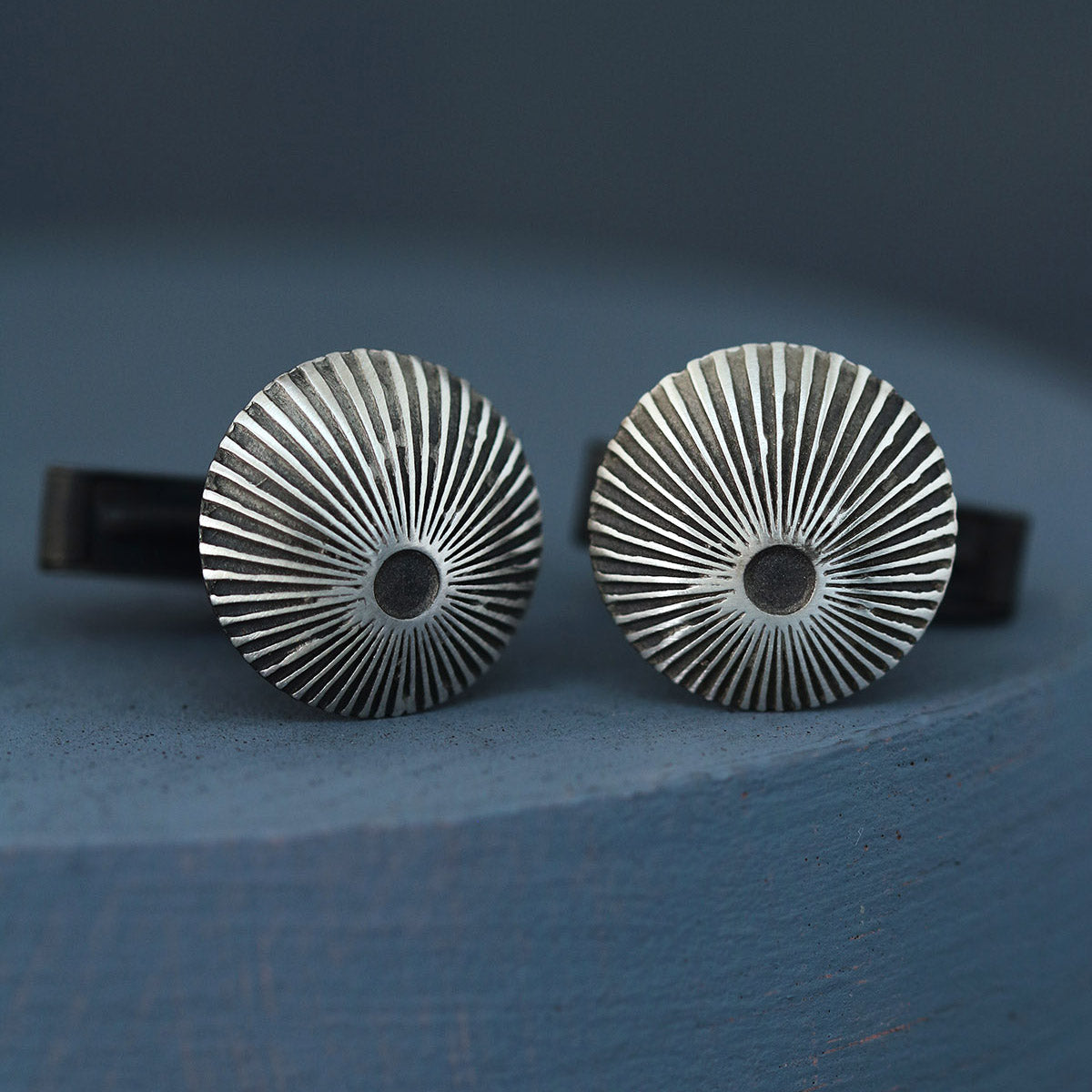 Detailed close-up of engraved silver and black cufflinks on deep blue background, thoughtful luxury cufflink gift for husband or partner.