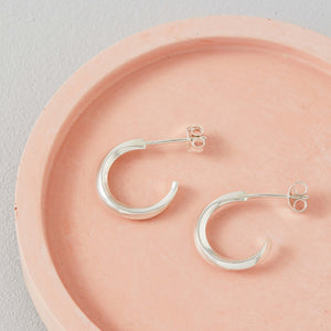 Close up of silver hoop stud earrings on a pink dish showing sculpted shape, sterling silver hoop earrings for women