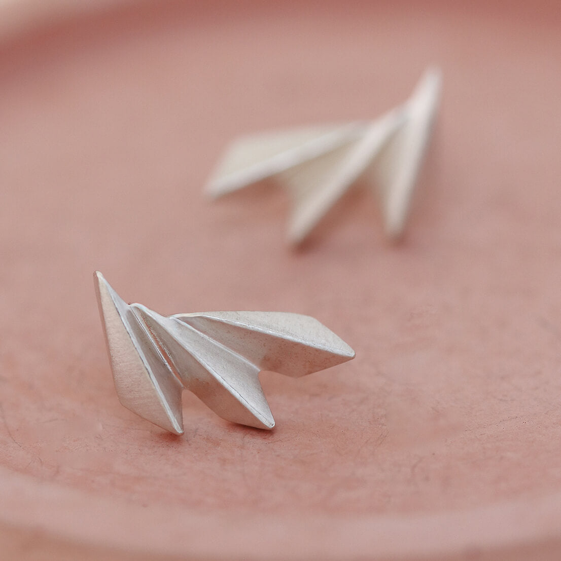 Overhead shot of art deco fan earrings on a pink dish showing symmetry and polish.