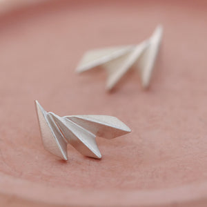 Overhead shot of art deco fan earrings on a pink dish showing symmetry and polish.