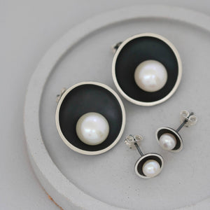 Comparison of black pearl stud earrings showing original and larger size side by side on grey dish