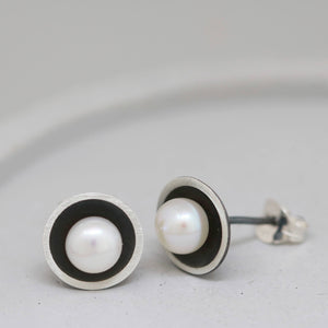 Black pearl earrings displayed on a grey dish with focus on the reflective pearl against the dark oxidised interior