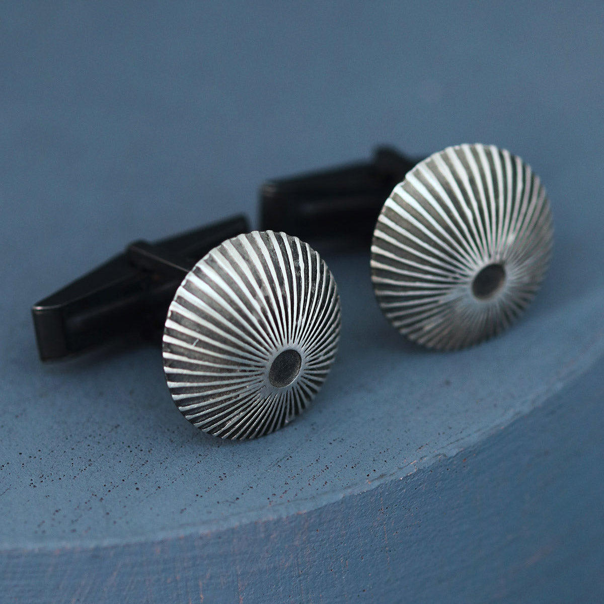 Angled view of silver and black cufflinks on deep blue background, stylish gift for man who loves unique mens luxury cufflinks.