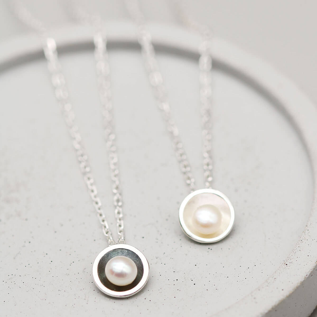 Black pearl pendant necklace beside the polished sterling silver version, highlighting the contrast between the two handcrafted finishes.
