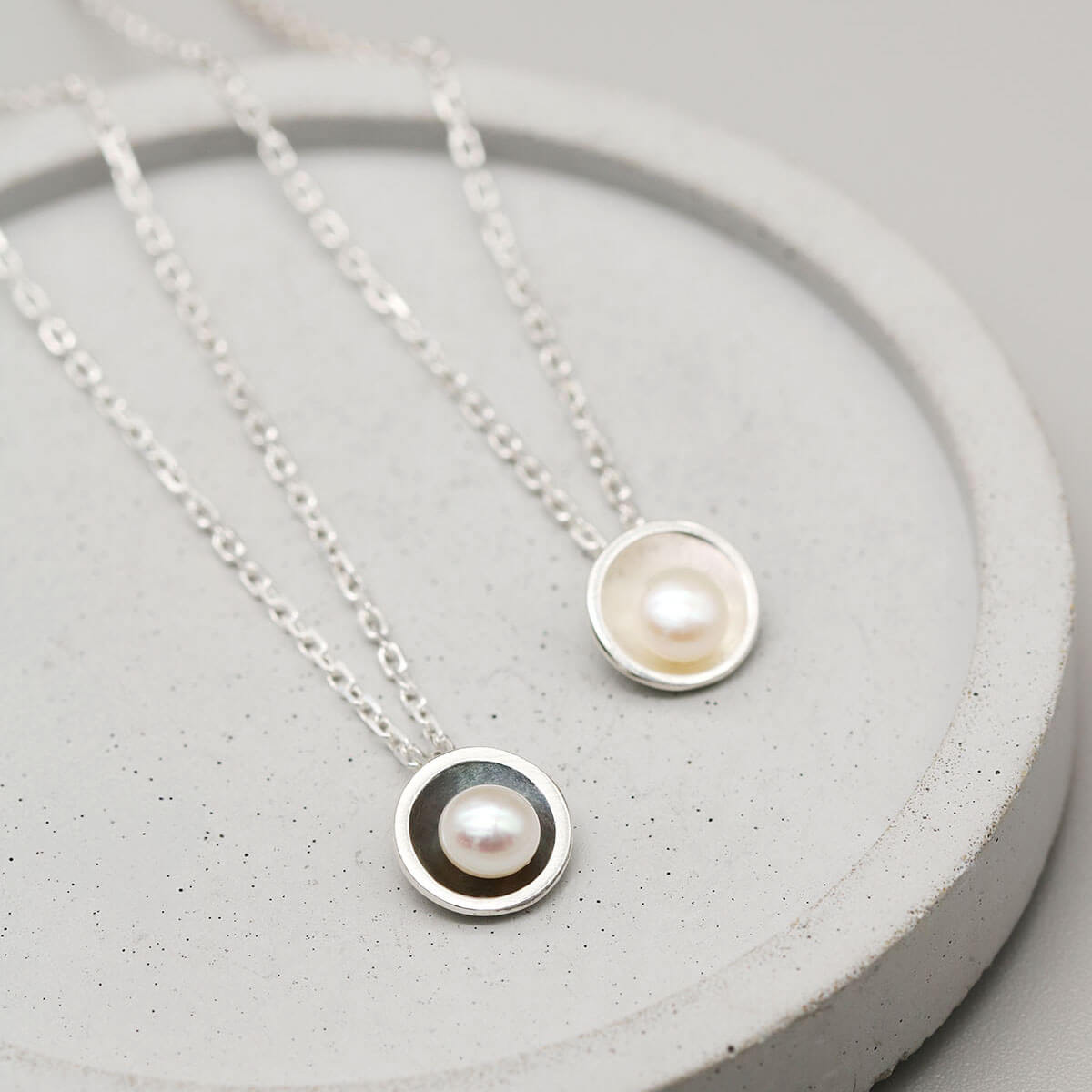 Oxidised sterling silver pearl pendant necklace displayed alongside the matching polished silver pearl pendant for comparison.
