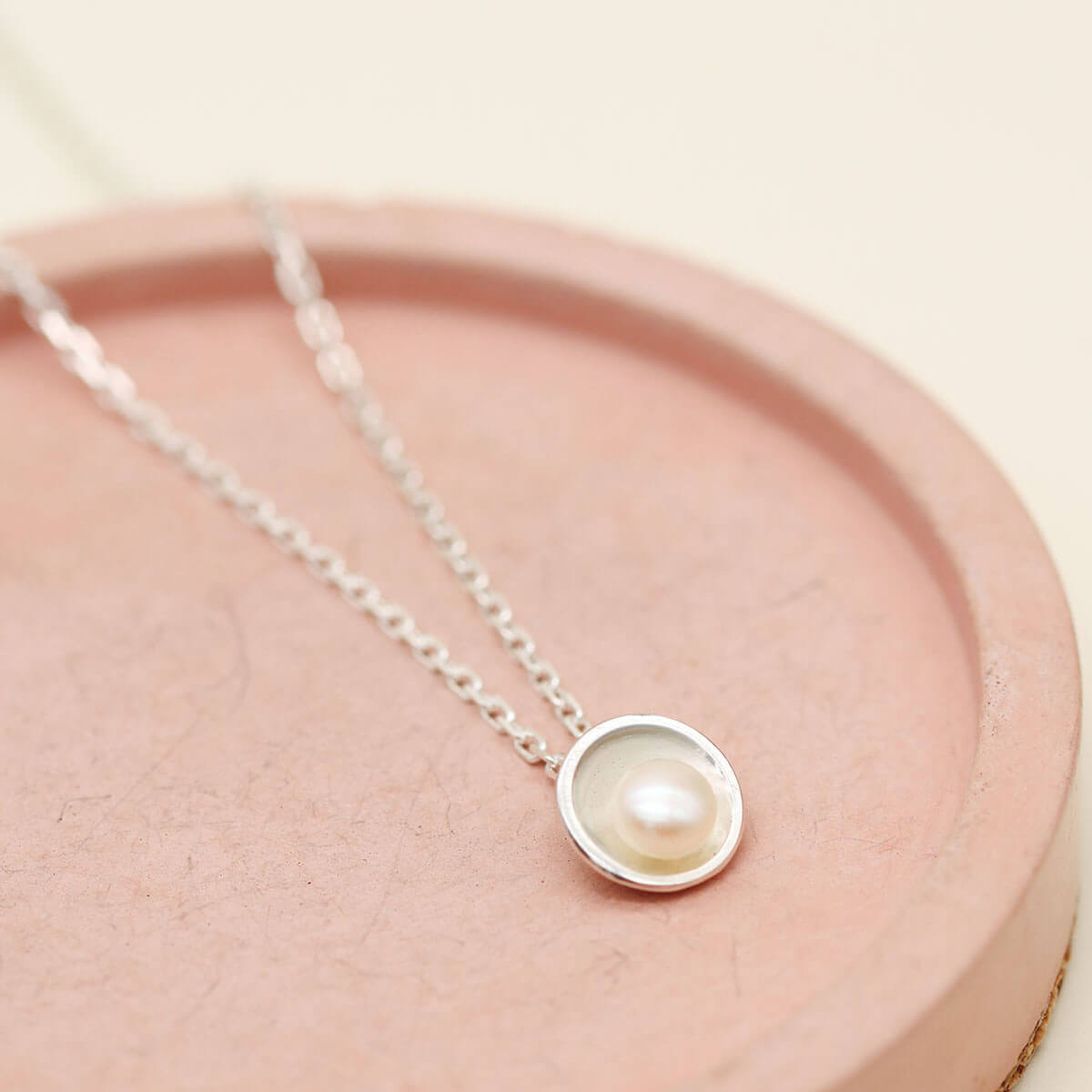 Sterling silver pendant with pearl on an 18-inch diamond cut oval trace chain, photographed on a pink ceramic dish.