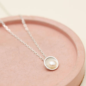 Sterling silver pendant with pearl on an 18-inch diamond cut oval trace chain, photographed on a pink ceramic dish.