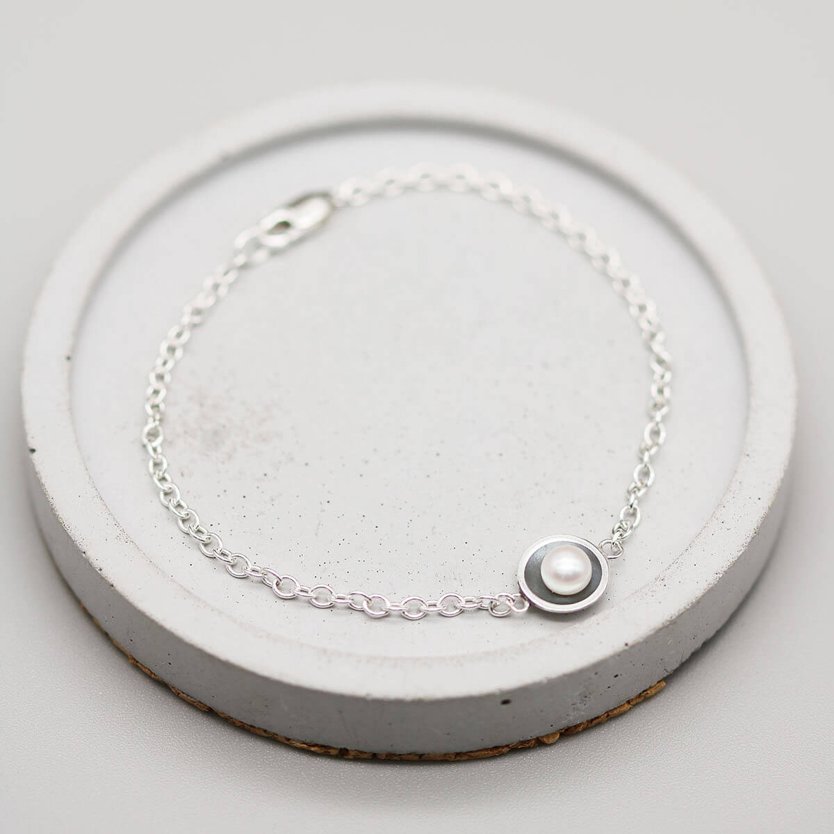 Black pearl bracelet handcrafted in sterling silver with a genuine freshwater pearl on a grey ceramic dish.