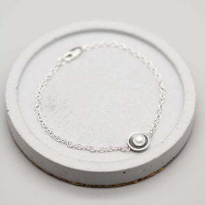 Black pearl bracelet handcrafted in sterling silver with a genuine freshwater pearl on a grey ceramic dish.