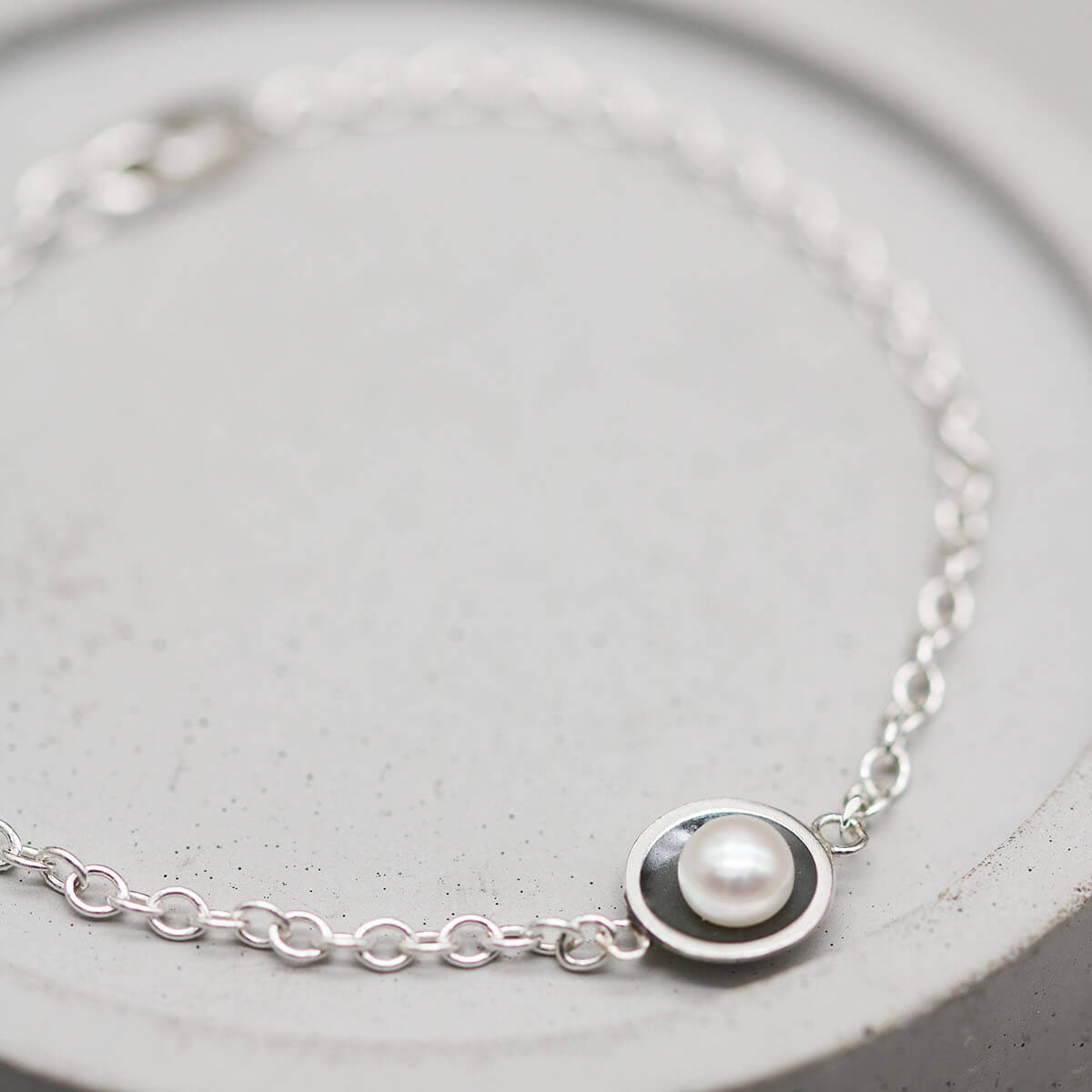 Handmade pearl and sterling silver bracelet with oxidised pearl setting and genuine freshwater pearl displayed on a grey dish.