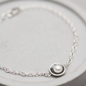 Handmade pearl and sterling silver bracelet with oxidised pearl setting and genuine freshwater pearl displayed on a grey dish.