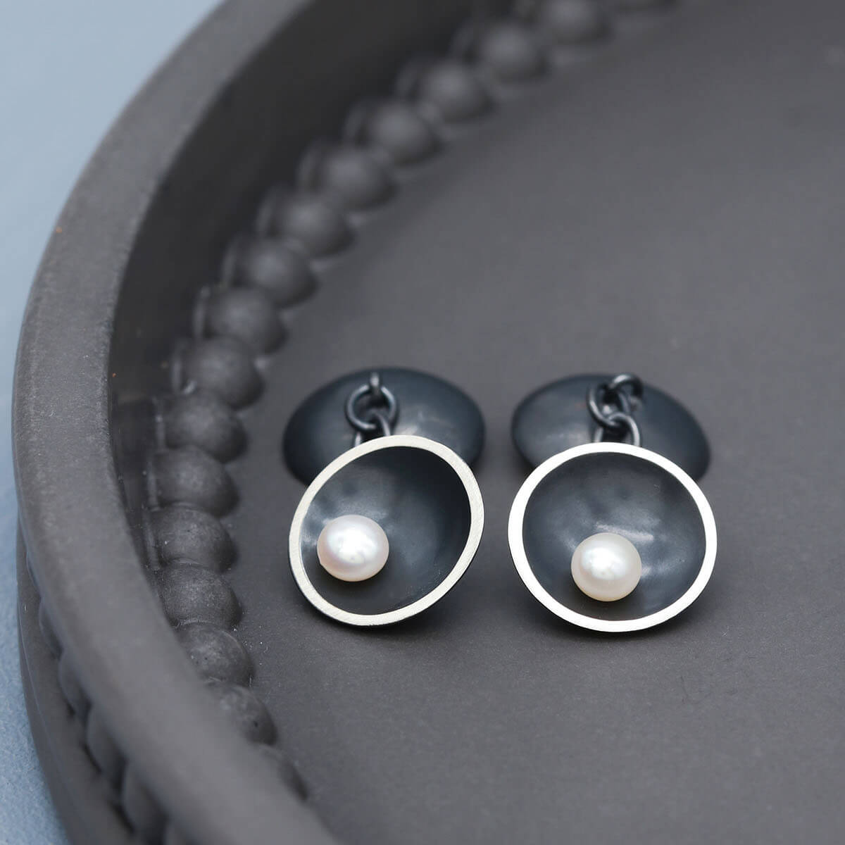 Black double-sided cufflinks with freshwater pearls displayed on a dark grey background.