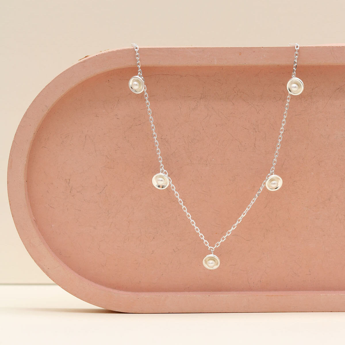 Handmade sterling silver pearl chain necklace with five genuine freshwater pearls displayed on a pink ceramic dish.