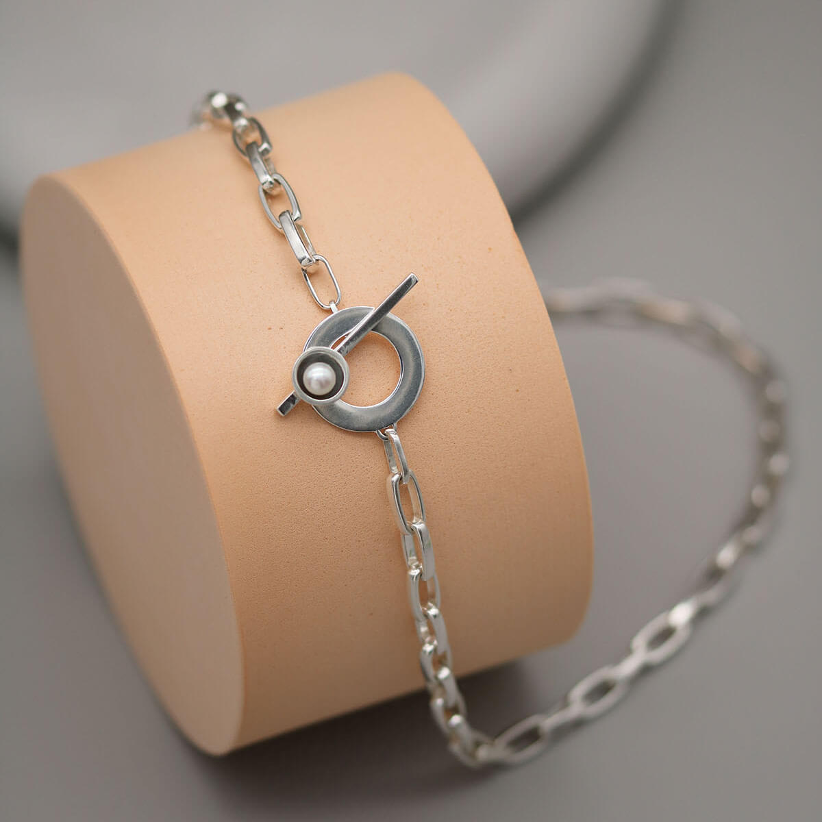 Sterling silver pearl chain necklace with statement T-bar clasp and genuine freshwater pearl displayed on a pink circular plinth against a grey background.