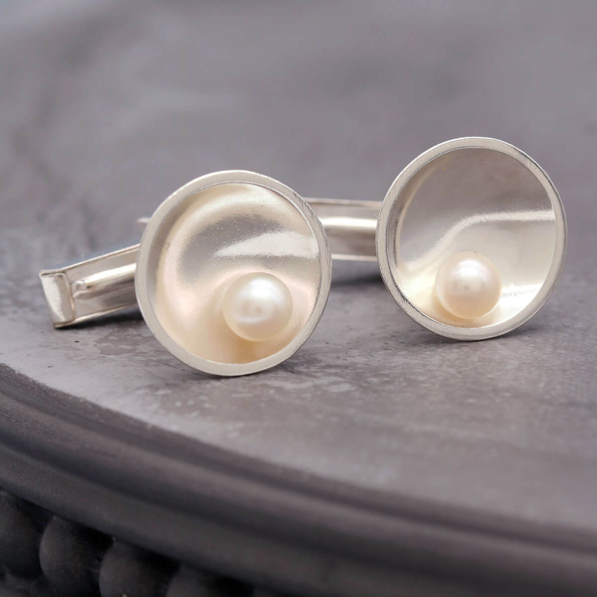 Handmade sterling silver pearl cufflinks for men with genuine freshwater pearls on a dark grey dish.
