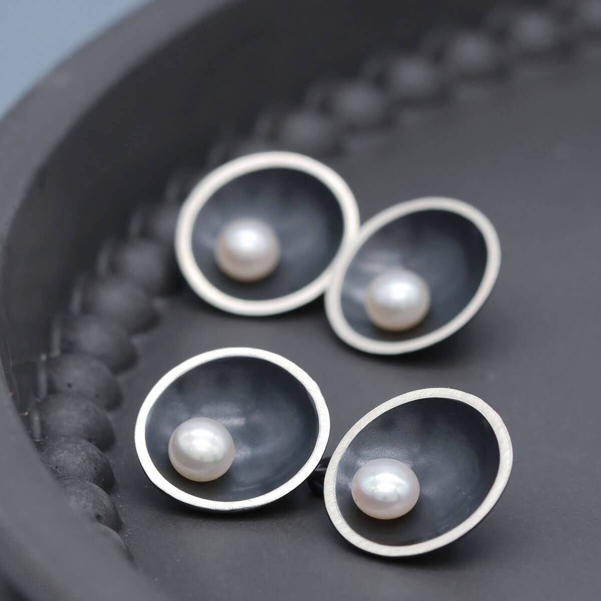 Handmade black double-sided pearl cufflinks in oxidised sterling silver with genuine freshwater pearls on a dark grey dish.
