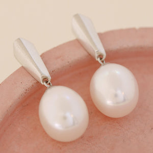 Pair of silver dangle pearl earrings resting on a pink dish, emphasising the elegant drop design and polished sterling silver finish.