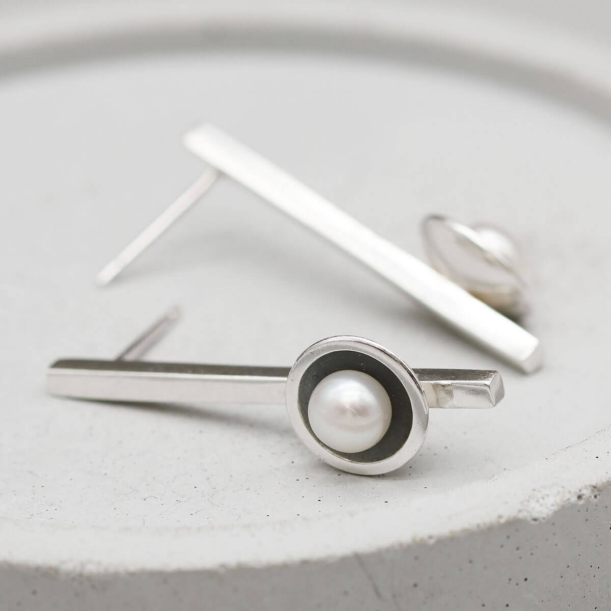 Elegant long drop pearl earrings in oxidised sterling silver shown on a grey ceramic dish.