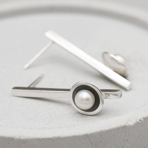 Elegant long drop pearl earrings in oxidised sterling silver shown on a grey ceramic dish.