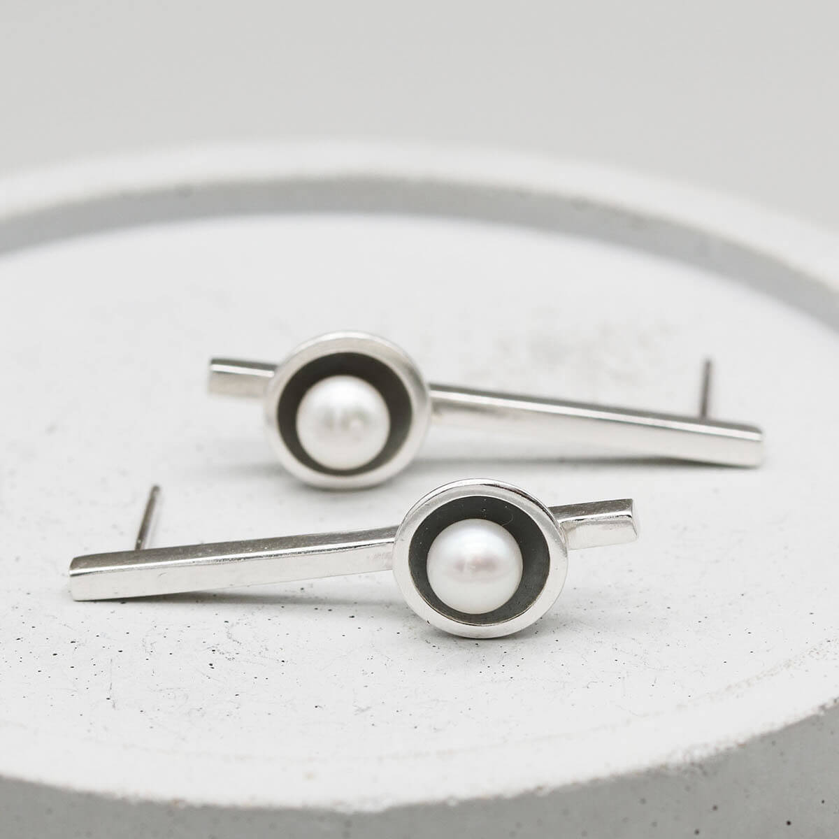 Long drop pearl earrings handcrafted from oxidised sterling silver with luminous freshwater pearls on a grey dish.