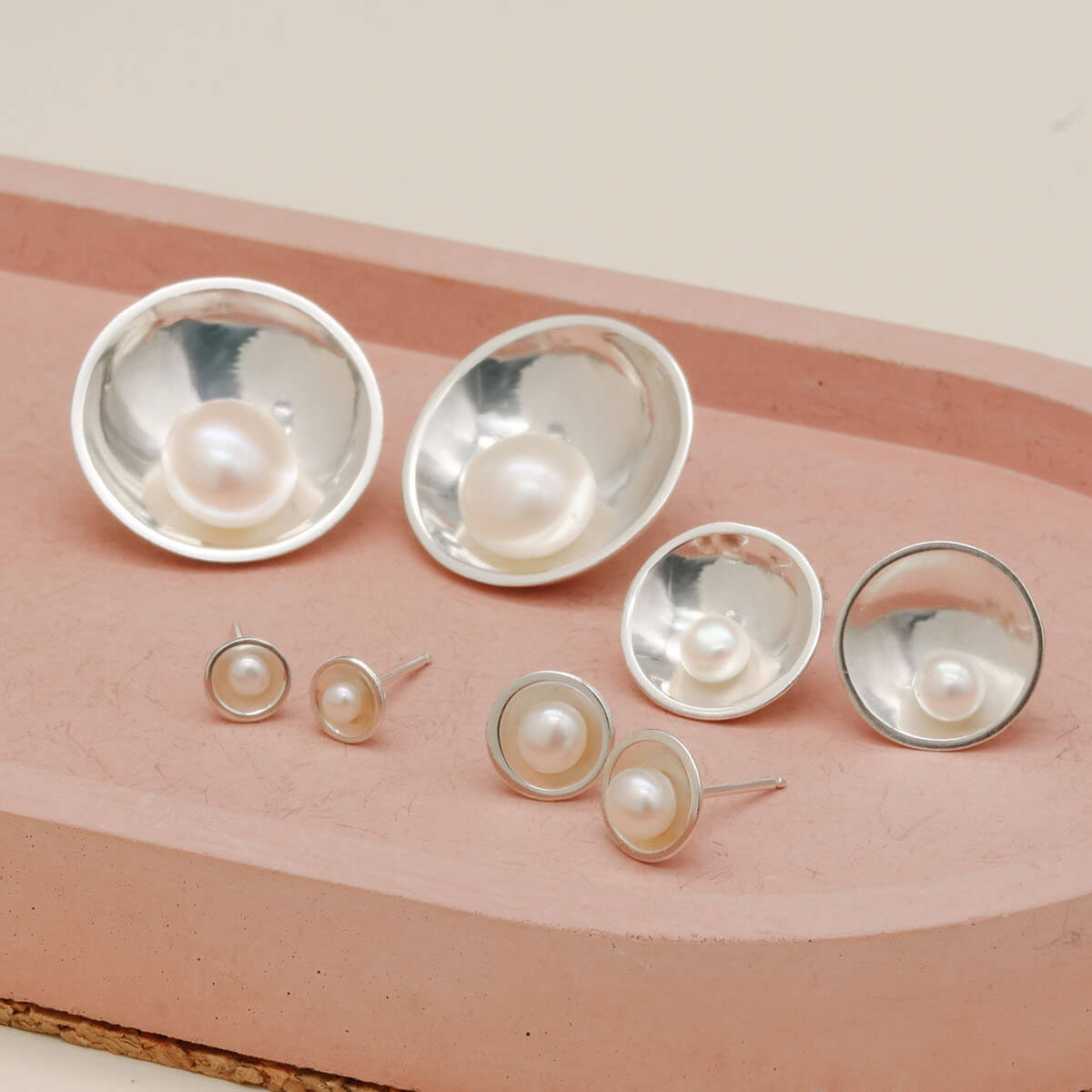 Four sizes of handmade sterling silver pearl stud earrings displayed together, including Petite, Classic, Signature and Statement designs.