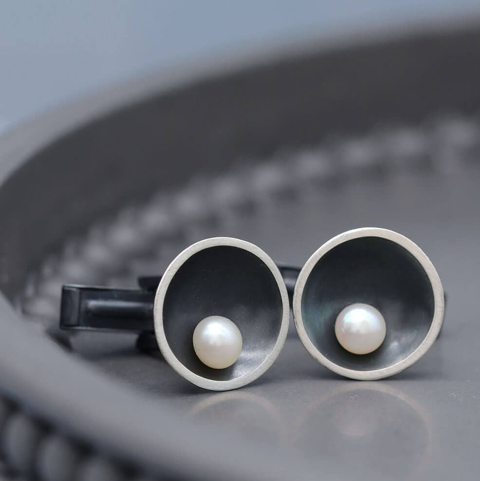 Men's black pearl cufflinks in sterling silver displayed on a dark grey background.