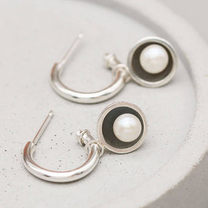 Handmade black pearl hoop earrings with removable freshwater pearl charms displayed on a grey ceramic dish.