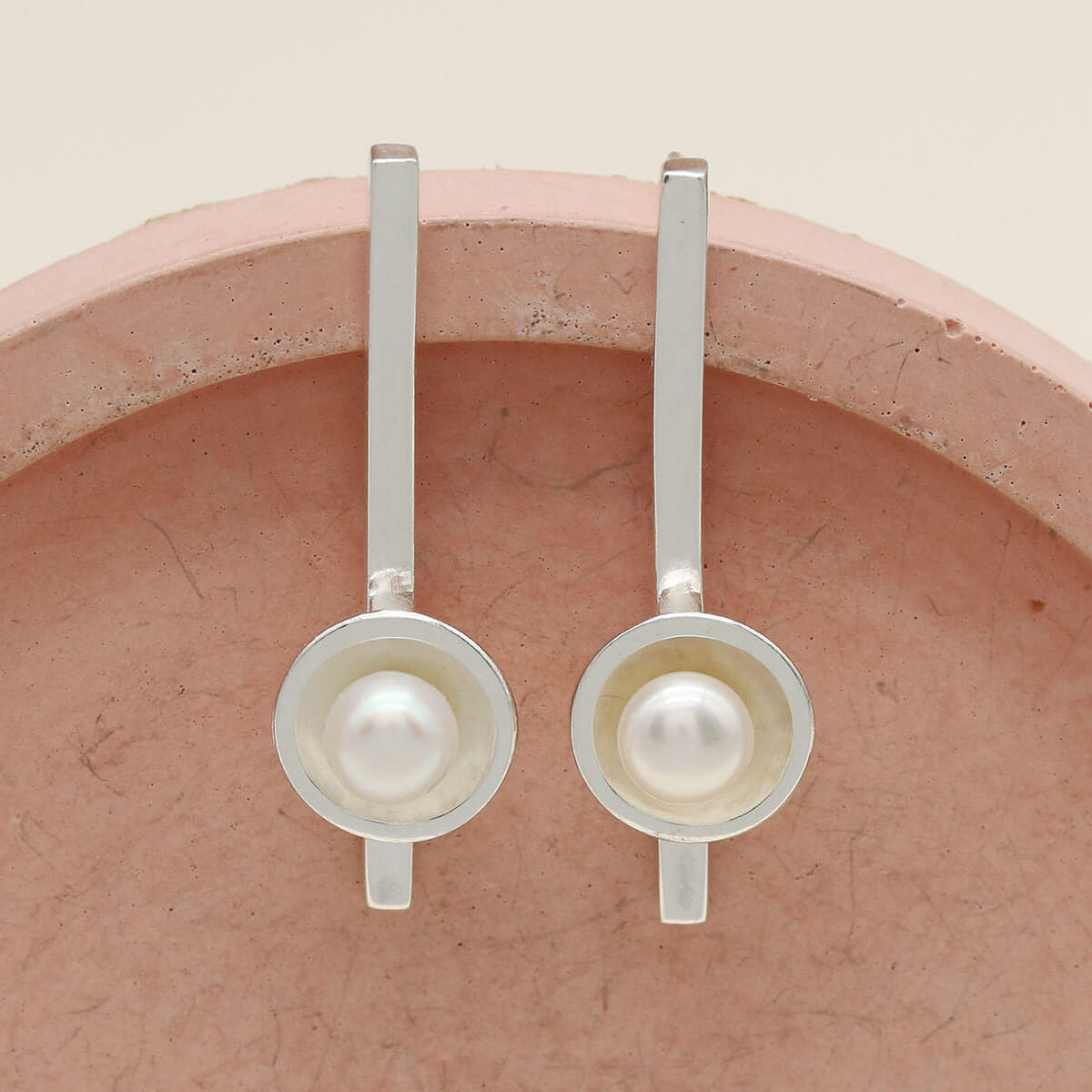 Handmade sterling silver long pearl earrings with genuine freshwater pearls displayed on a pink ceramic dish.