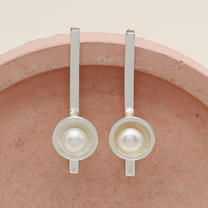 Handmade sterling silver long pearl earrings with genuine freshwater pearls displayed on a pink ceramic dish.