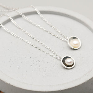 Handcrafted black and silver pearl pendant necklaces with genuine freshwater pearls shown together on a dark grey dish.
