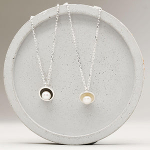 Comparison of polished sterling silver and oxidised black pearl pendant necklaces, each handmade with a single freshwater pearl.