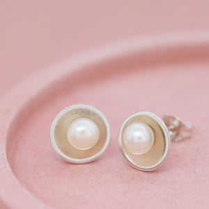 Top-down image of sterling silver pearl stud earrings on pastel pink background, showcasing their minimalist bridal style.