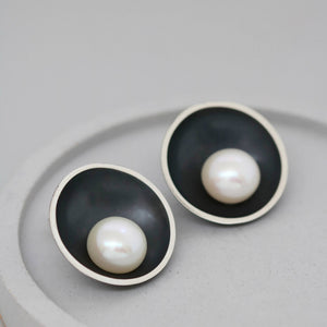 Large black pearl stud earrings displayed on a grey ceramic dish