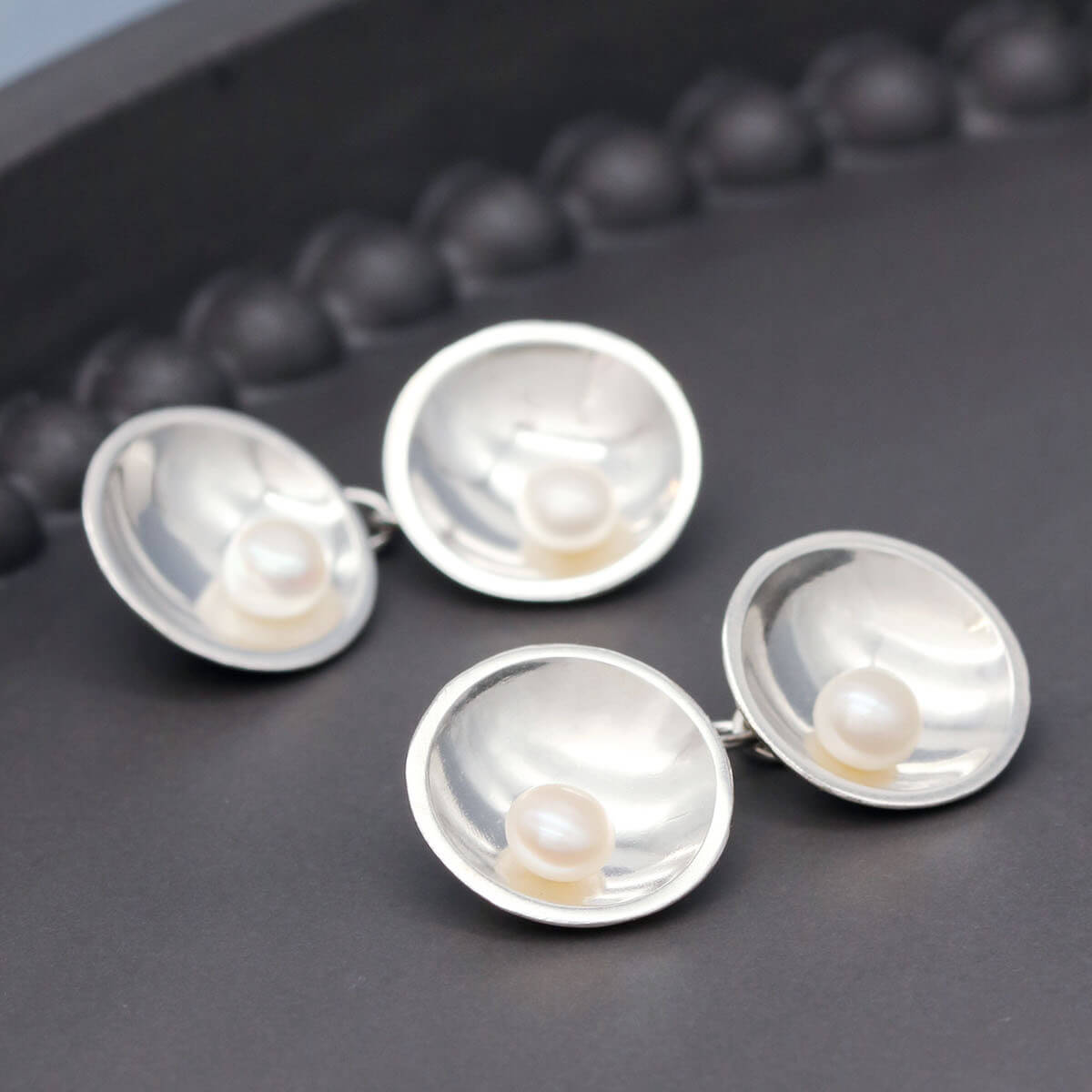 Sterling silver double-sided pearl cufflinks displayed on a dark grey background, showcasing pearls on both sides.