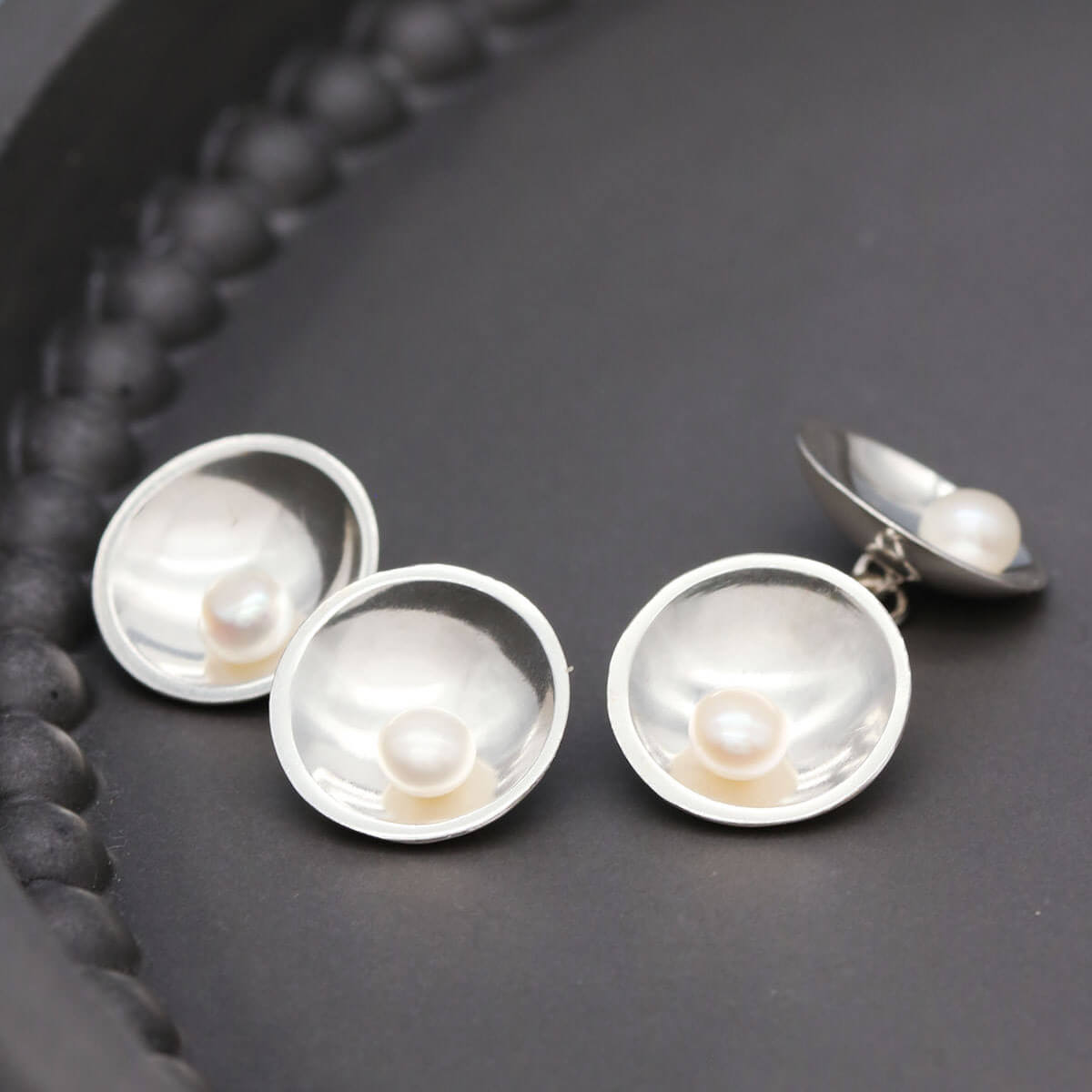 Close up of men's pearl cufflinks showing traditional silversmithing craftsmanship and chain-linked construction.