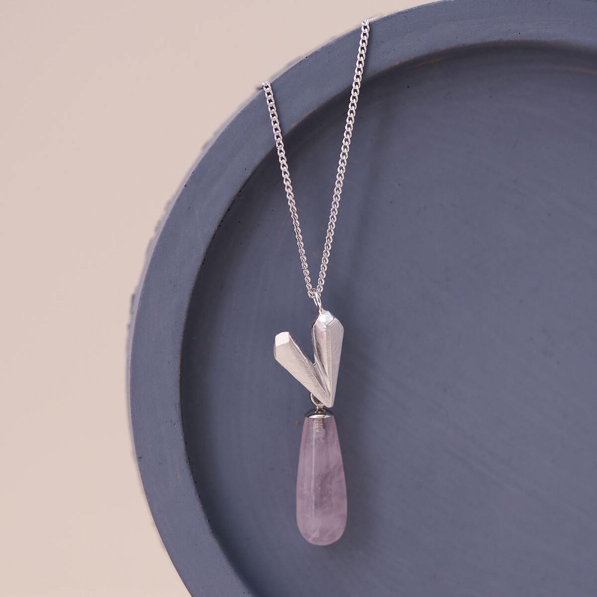 Sterling silver heart necklace with pink quartz heart pendant displayed on a blue dish, featuring a faceted heart charm and soft blush gemstone.