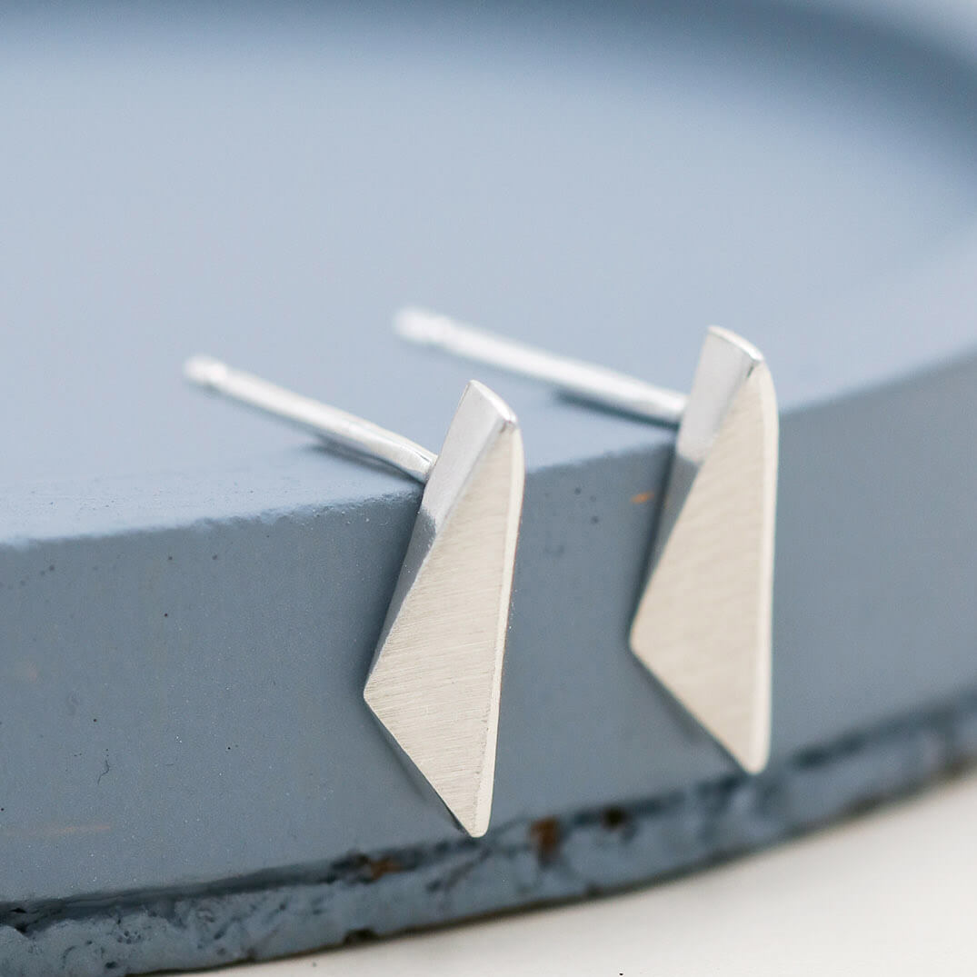 Kite-shaped sterling silver stud earrings, small everyday earrings and thoughtful jewellery gift for her, on a deep blue dish