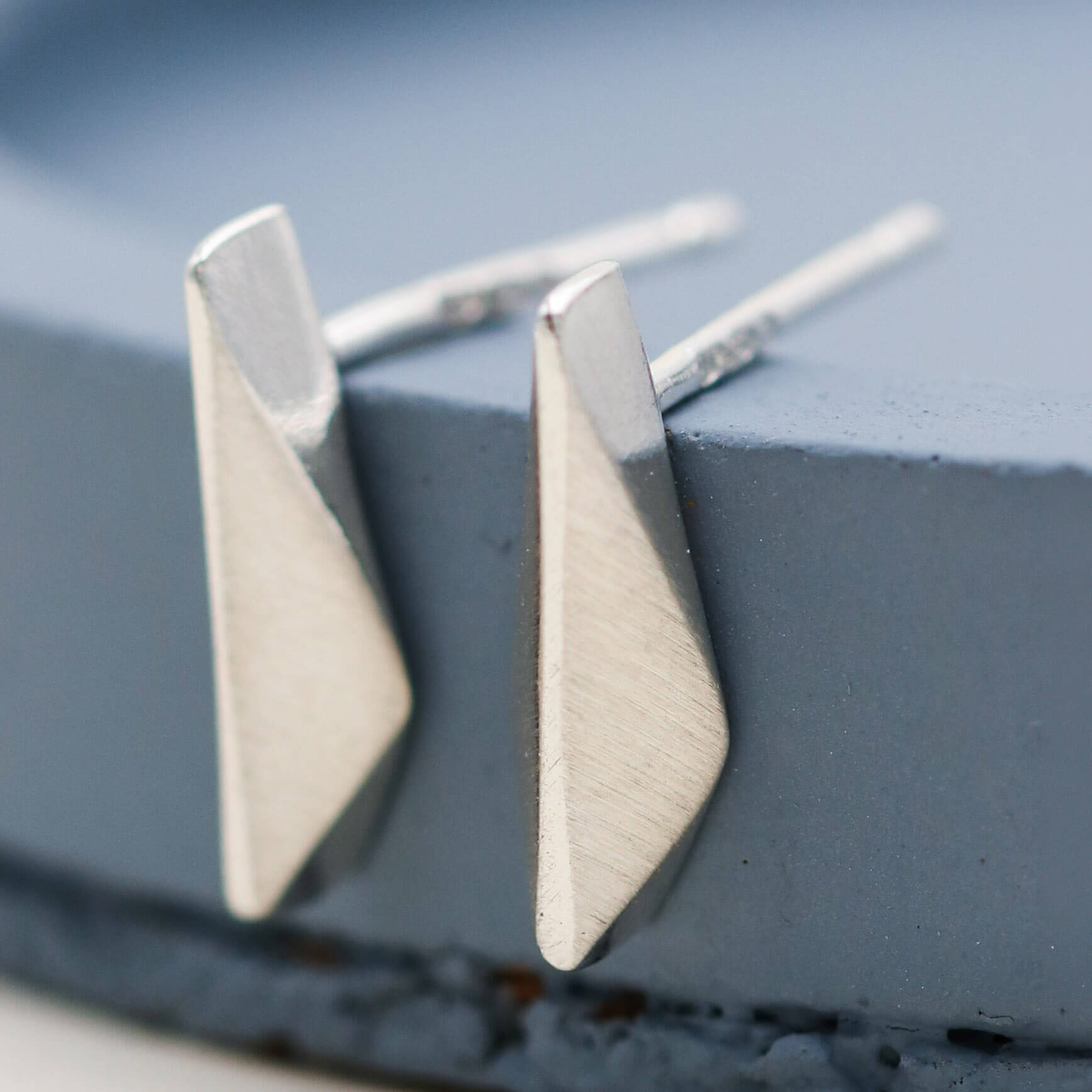 Small silver studs handmade in sterling silver, delicate kite-shaped earrings for everyday wear on a deep blue dish