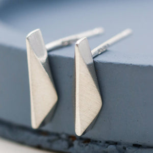 Small silver studs handmade in sterling silver, delicate kite-shaped earrings for everyday wear on a deep blue dish