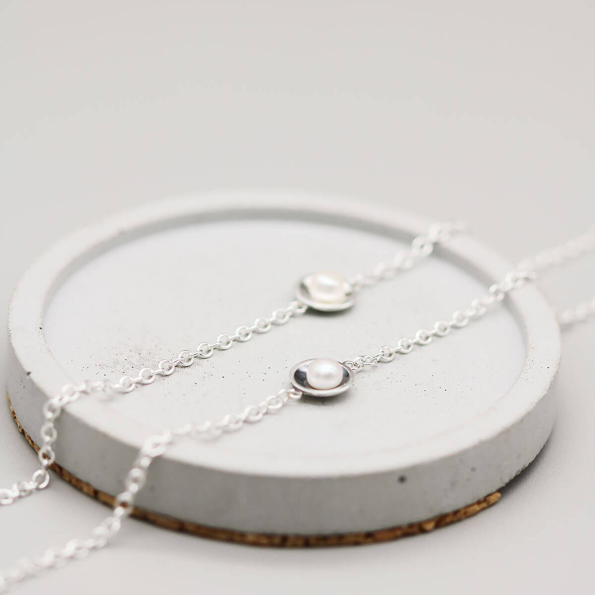Handmade sterling silver pearl bracelets in polished and oxidised finishes displayed side by side on a grey dish.